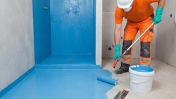 Man waterproofing bathroom surface with bucket and roller