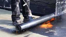 Person waterproofing roof using a torch